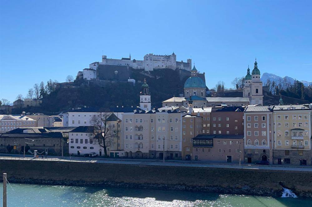 Panoramablick auf die historische Stadt Salzburg mit Fluss, Gebäuden und der imposanten Festung Hohensalzburg.