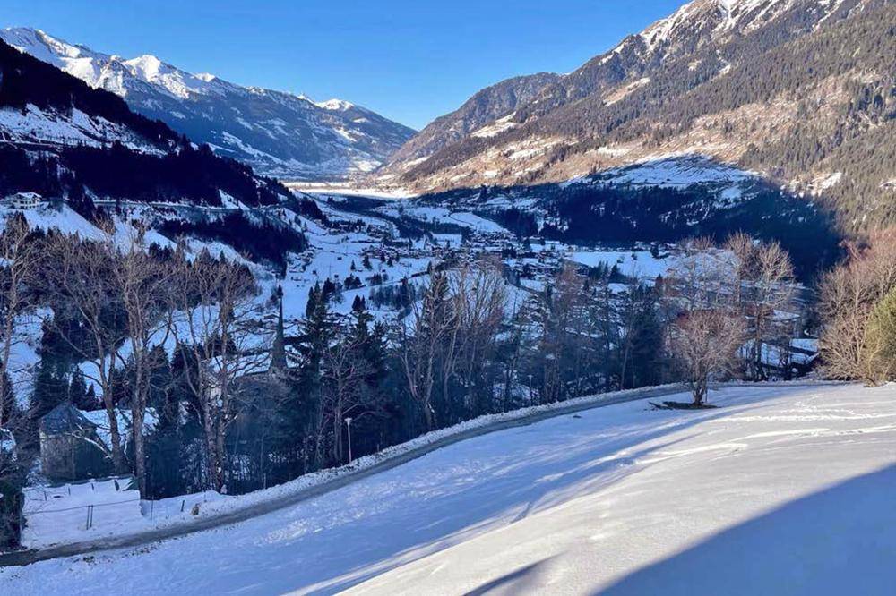 Weitläufiger Blick über ein schneebedecktes Tal mit Bergen und einem kleinen Dorf in der Ferne.