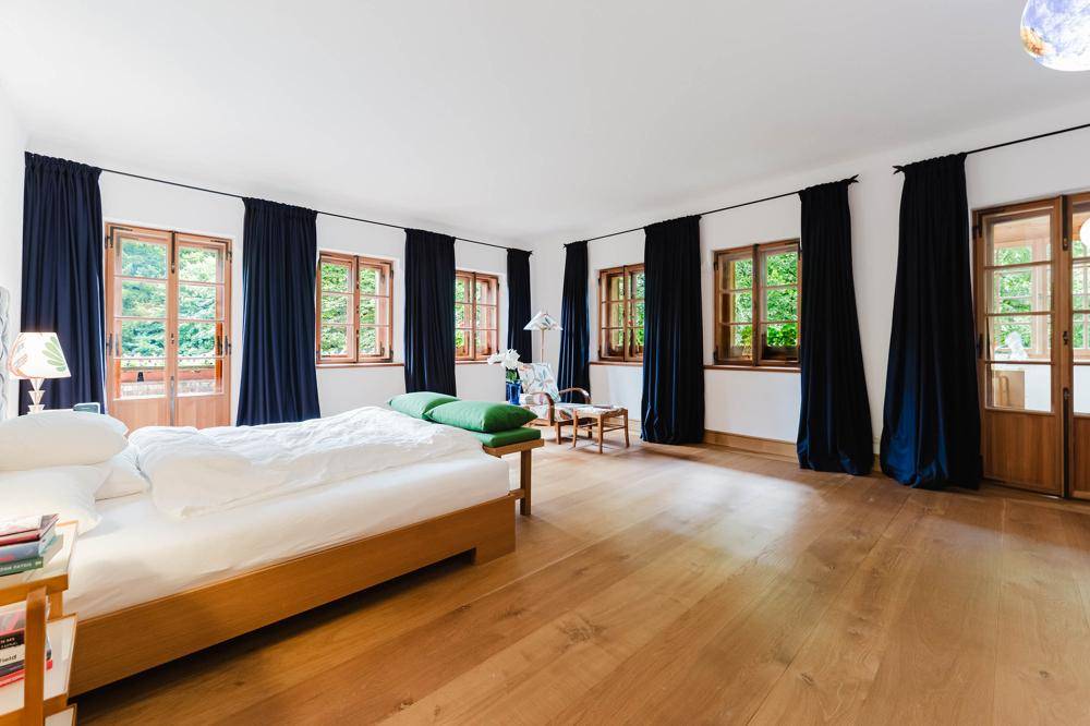 Helles Schlafzimmer mit Holzboden, großzügigen Fenstern und Zugang zu einem Balkon oder Garten.