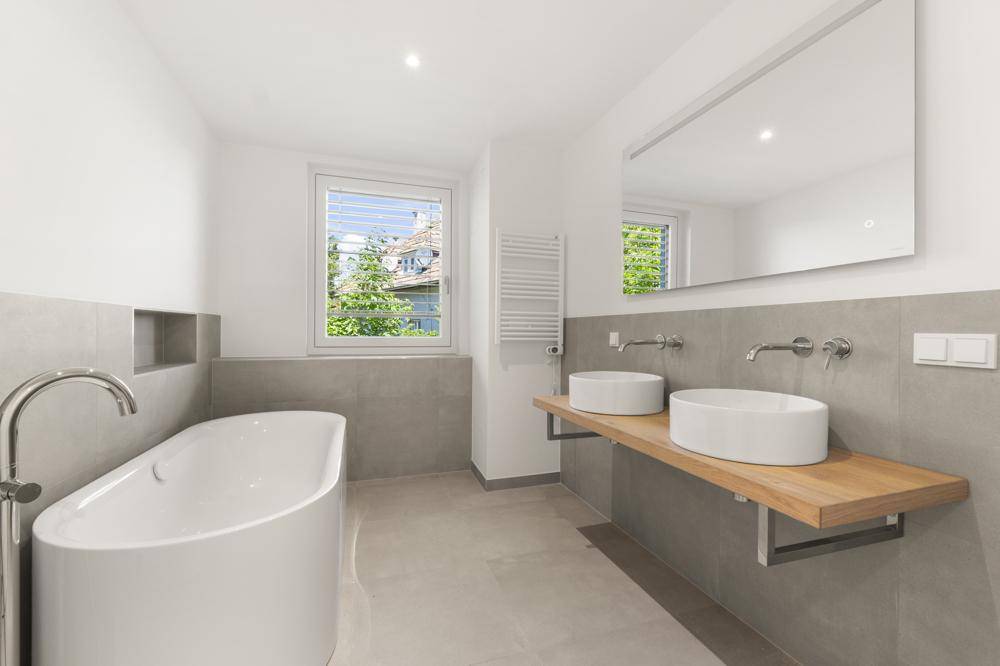 Modernes Badezimmer mit freistehender Badewanne, Doppelwaschbecken und großen Fliesen.