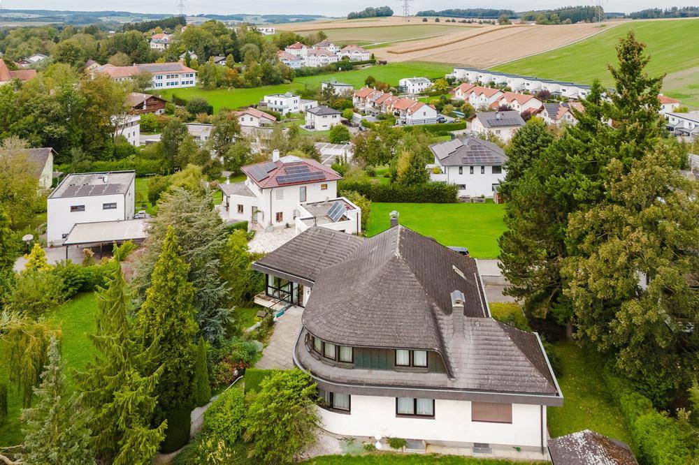 Architektonisch interessantes Haus mit geschwungener Form und dunklem Dach, eingebettet in eine grüne Landschaft.
