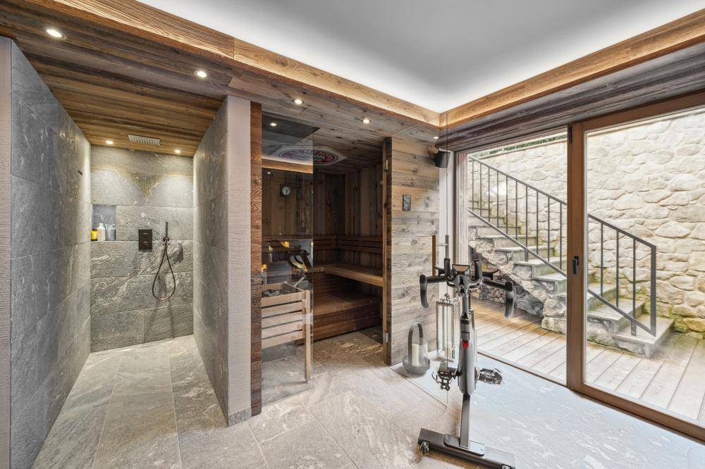 Exklusiver Wellnessbereich mit Sauna, moderner Dusche und Fitnessgerät, mit Zugang zum Außenbereich.