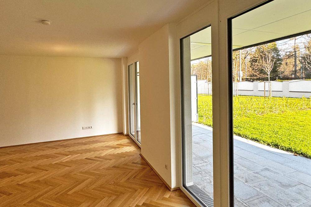 Heller Wohnraum mit Fischgrätparkett und großen Glasfronten zum Garten und zur Terrasse.