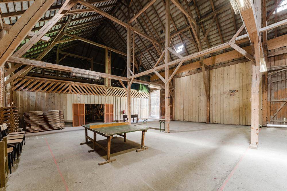 Geräumige Scheune mit sichtbaren Holzbalken und Betonboden, genutzt als Mehrzweckhalle.
