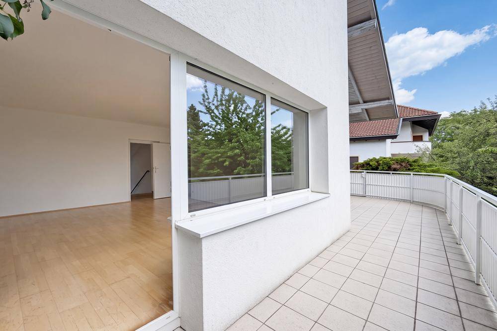 Heller Wohnbereich mit Parkettboden und direktem Zugang zu einer großen gefliesten Terrasse.