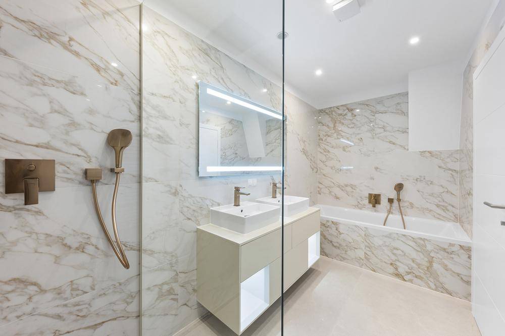 Modernes Badezimmer mit Marmorfliesen, Doppelwaschbecken und integrierter Badewanne und Dusche.