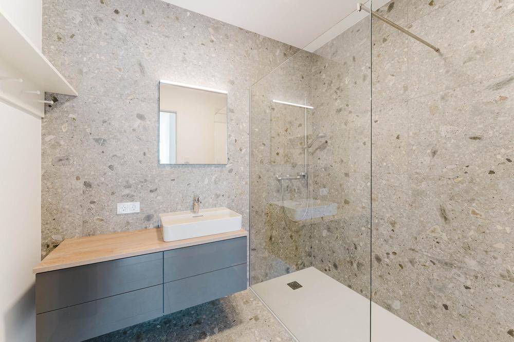 Modernes Badezimmer mit großformatigen Fliesen, schwebendem Waschtisch und einer geräumigen begehbaren Dusche.