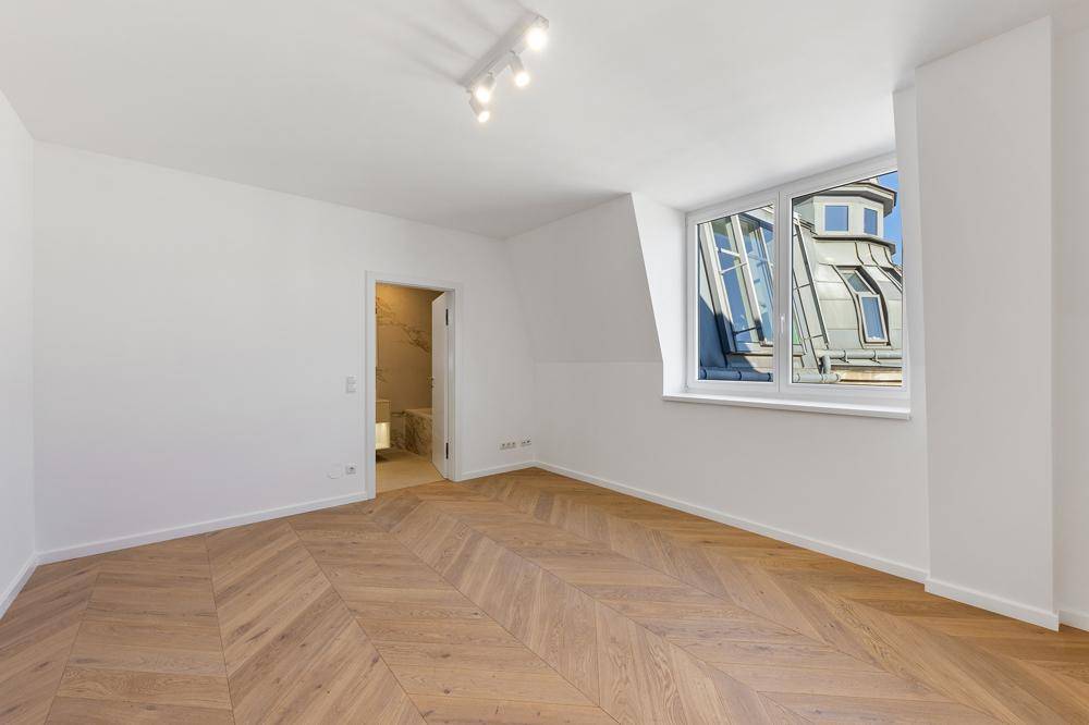 Schlafzimmer mit Fischgrätparkett, Dachschräge und Fenster mit Blick auf die umliegenden Dächer.