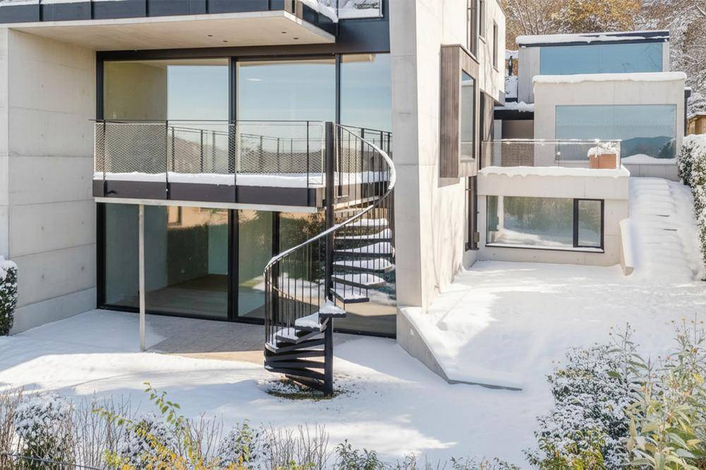 Moderne Architektur mit großen Glasflächen und einer eleganten Wendeltreppe, umgeben von einer verschneiten Landschaft.
