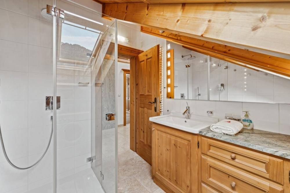 Modernes Badezimmer mit begehbarer Dusche, Holzwaschtisch und Dachfenster für natürliches Licht.