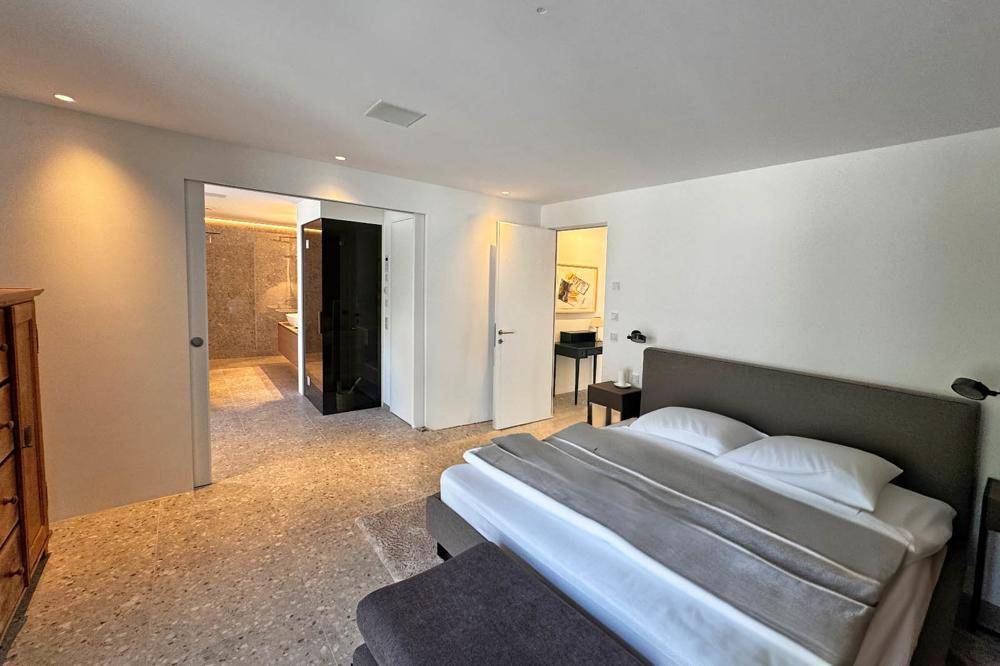 Helles Schlafzimmer mit Doppelbett und Zugang zu einem modernen Badezimmer.