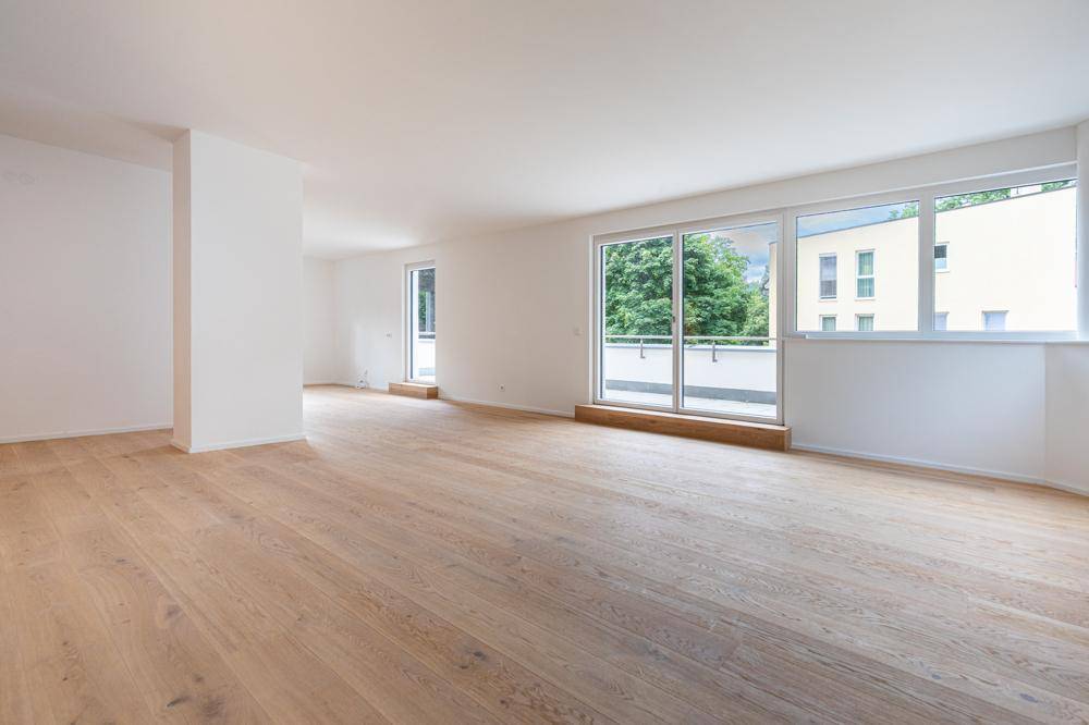 Heller, leerer Wohnbereich mit Eichenparkettboden und Zugang zu einem Balkon.