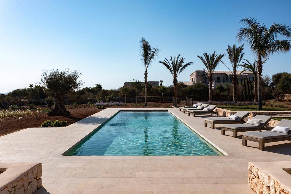 Langer, rechteckiger Pool mit Sonnenliegen und weitläufiger mediterraner Landschaft im Hintergrund.