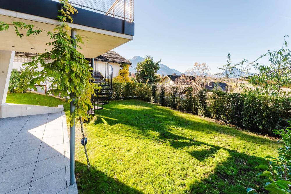 Gepflegter Garten mit Rasenfläche, Hecke und Blick auf die Berge.