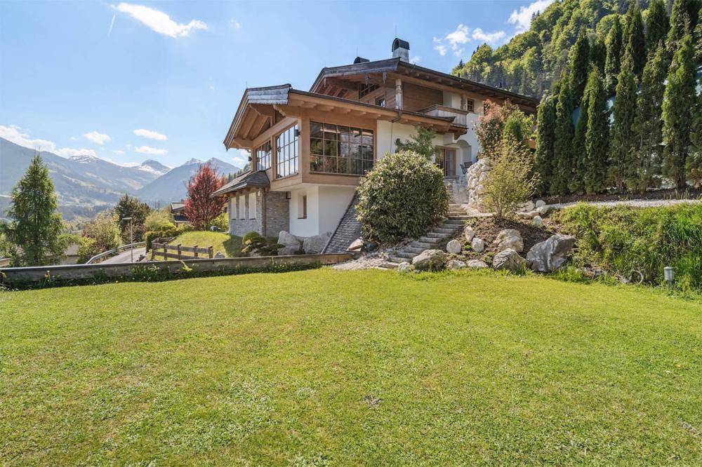 Alpines Chalet mit weitläufigem Rasenbereich und Panoramablick auf die umliegende Berglandschaft.