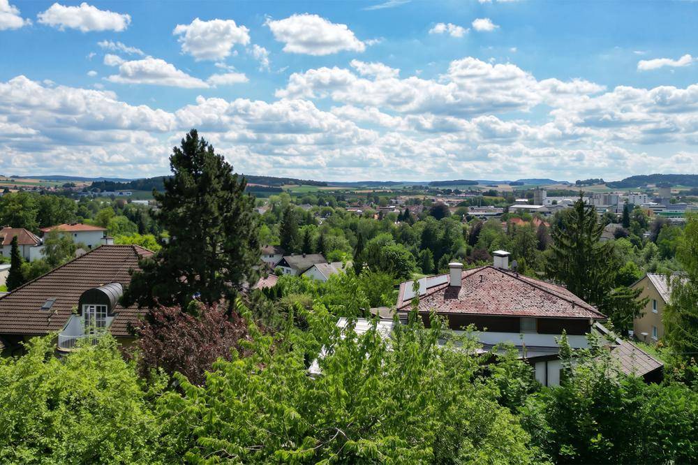 Weitläufiger Panoramablick über die Stadt und die umliegende grüne Landschaft unter blauem Himmel.