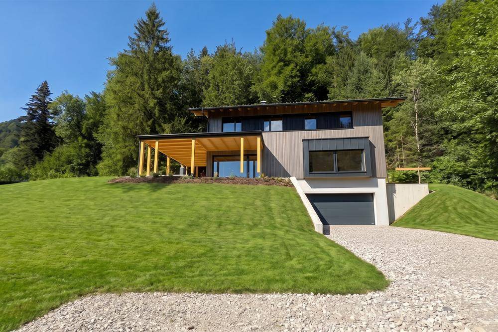 Zeitgenössisches Wohnhaus mit Holzverkleidung und großer Garage, eingebettet in eine bewaldete Hügellandschaft.