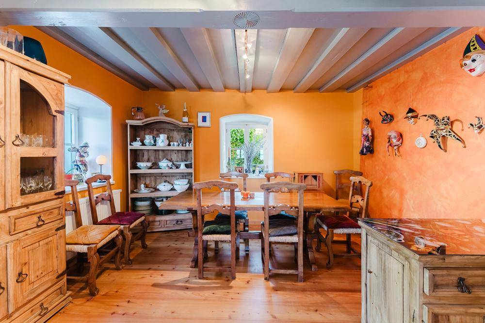 Rustikaler Essbereich mit Holztisch, passenden Stühlen und traditionellen Holzmöbeln, umgeben von orangefarbenen Wänden.