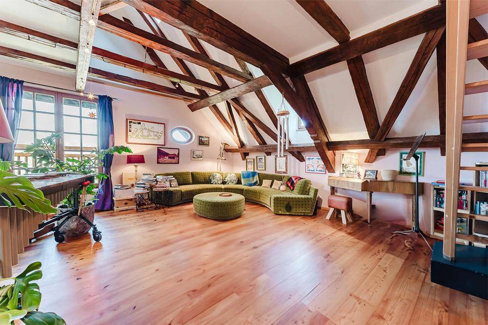 Großzügiger Wohnbereich im Dachgeschoss mit freiliegenden Holzbalken, Parkettboden und gemütlicher Sitzecke.