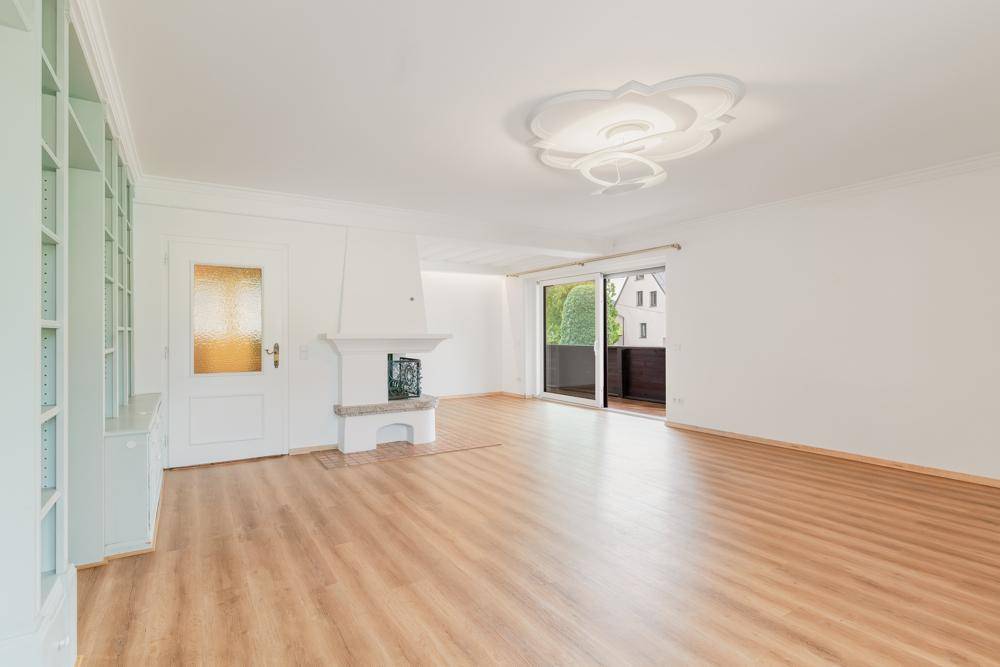 Helles Wohnzimmer mit Kamin, Laminatboden und Zugang zu einem Balkon mit Grünblick.
