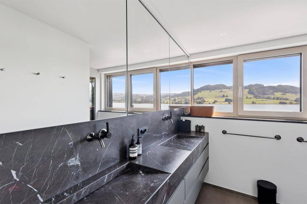 Modernes Badezimmer mit Doppelwaschbecken, dunklen Marmoroberflächen und Seeblick.