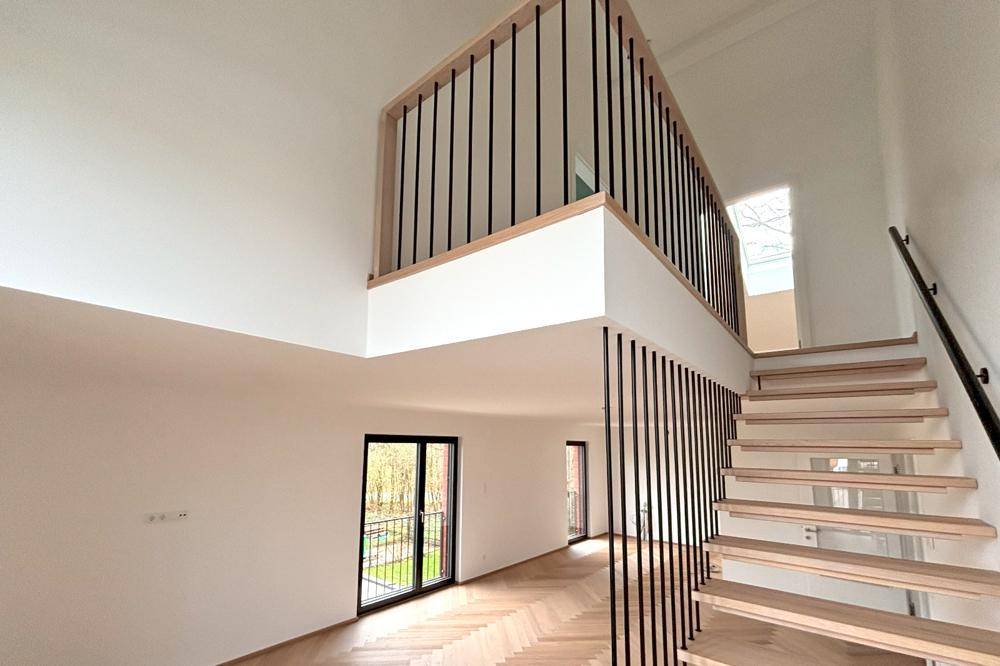 Offener Wohnbereich mit hoher Decke und Galerie, die den Blick nach draußen freigibt.