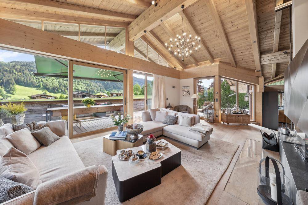 Helles Wohnzimmer mit hohen Holzdecken, großen Fenstern und Panoramablick auf die grüne Landschaft.