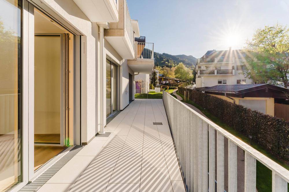 Langer, sonniger Balkon mit hellen Fliesen, Metallgeländer und Blick auf die Umgebung.