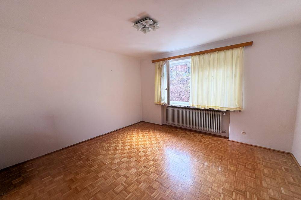 Helles Schlafzimmer mit Parkettboden, weiß gestrichenen Wänden und einem Fenster zur Natur.