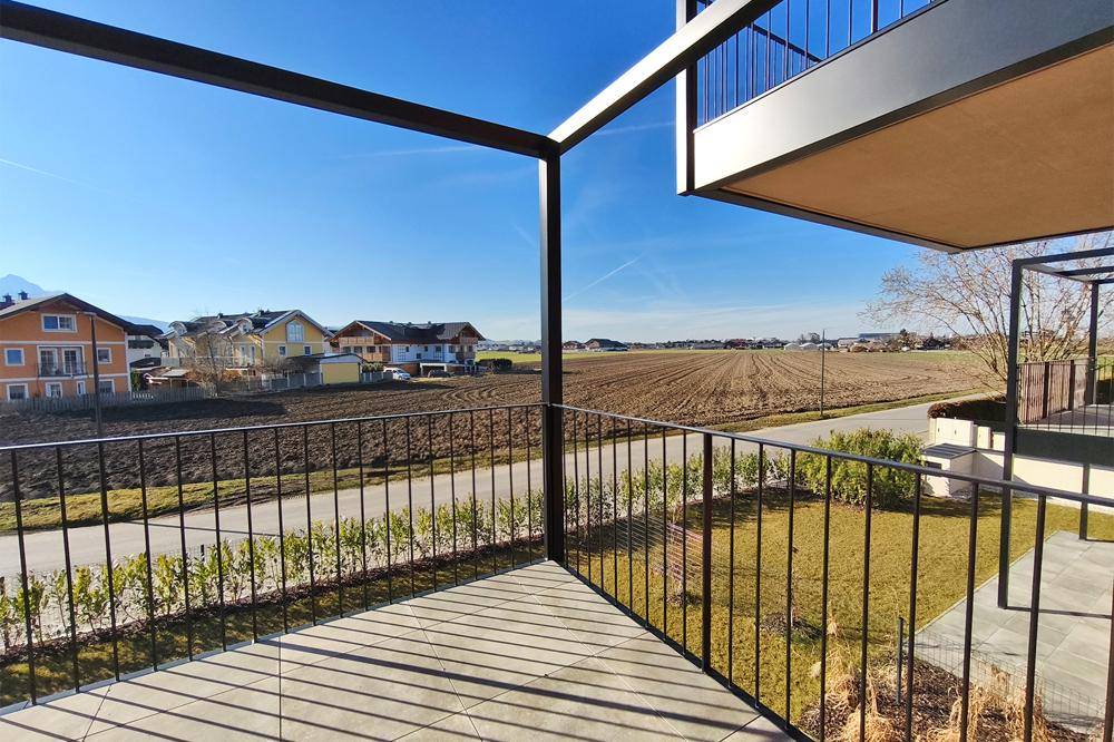 Balkon mit weitem Blick über Felder und die umliegende Wohnbebauung unter blauem Himmel.