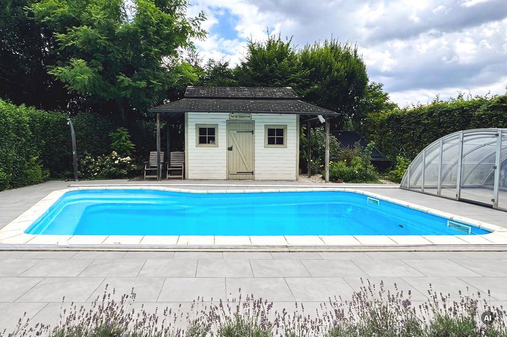 Großer Außenpool mit gepflasterter Terrasse und einem charmanten Poolhaus im Hintergrund.