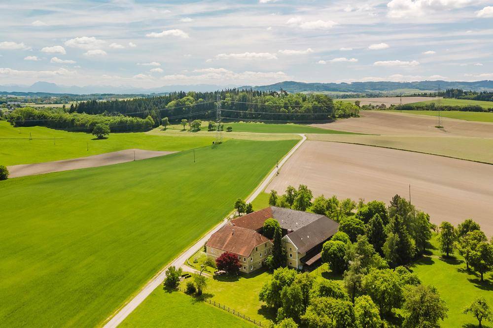 Weitläufige Luftaufnahme des Anwesens mit umliegenden Feldern, Wäldern und sanften Hügeln in der Ferne.