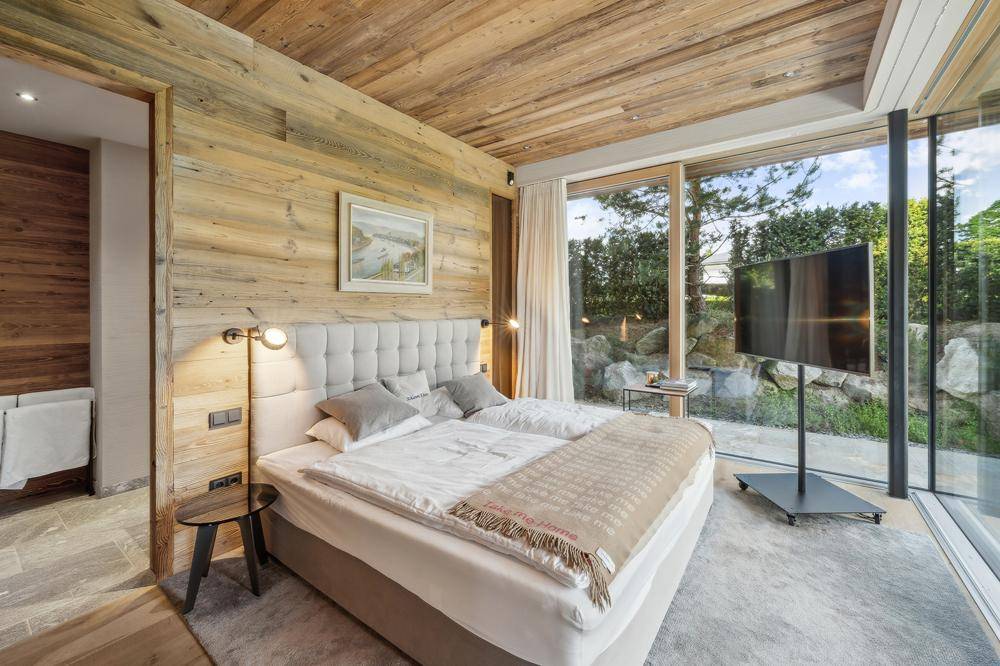 Modernes Schlafzimmer mit Holzwänden, großen Fenstern und direktem Zugang zum privaten Gartenbereich.