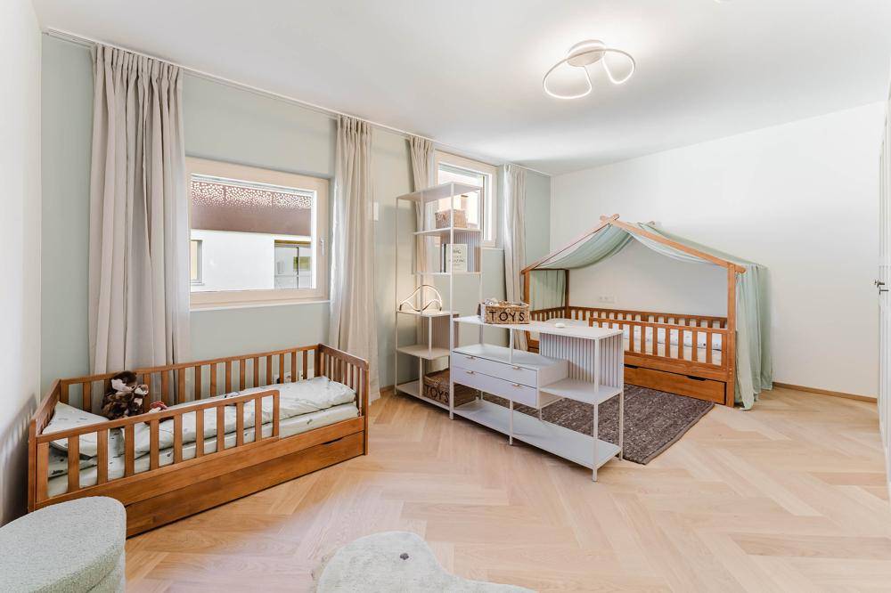 Kinderzimmer mit zwei Holzbetten, Parkettboden und hellen Wänden.