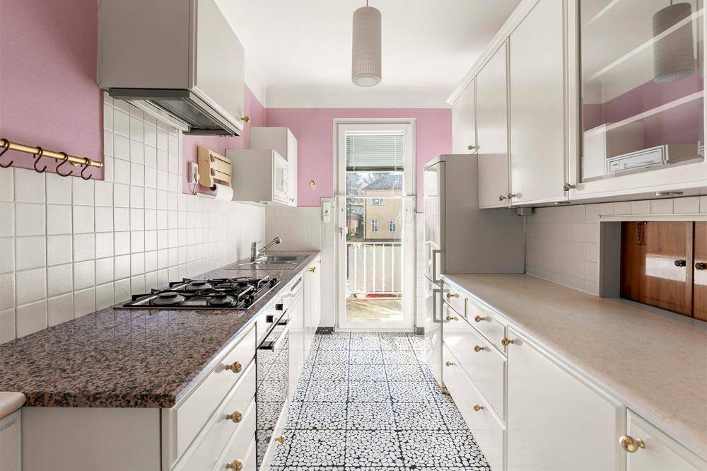 Schmale Küche mit rosa Wänden, weißen Schränken, Granitarbeitsplatte und Zugang zum Balkon.