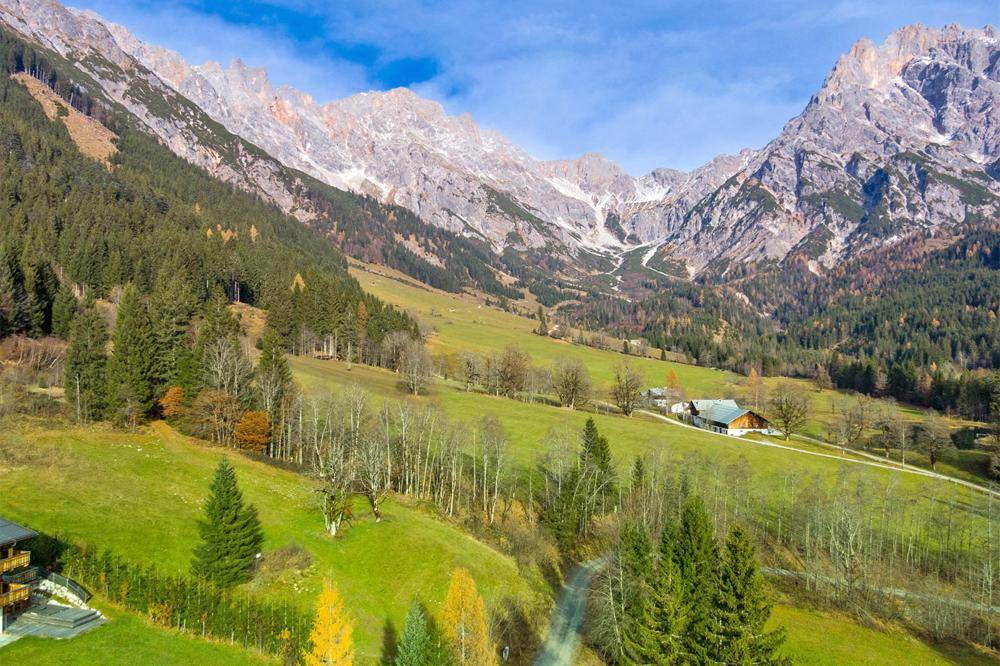 Panoramablick auf ein weites Tal mit grünen Wiesen, bewaldeten Hängen und imposanten Bergen im Hintergrund.
