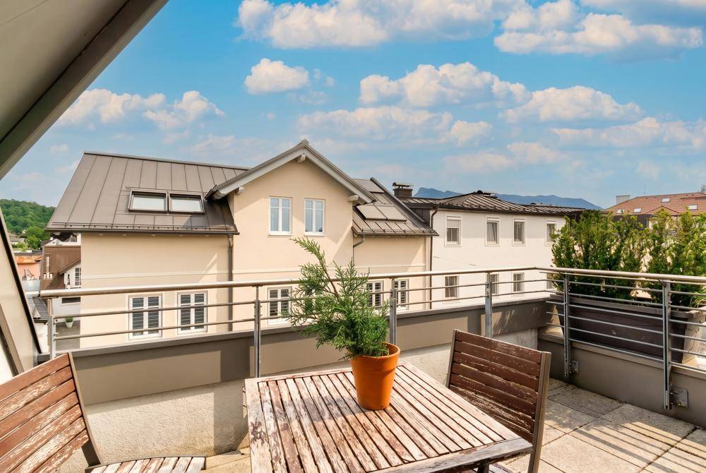 Geräumige Dachterrasse mit Holztisch und Stühlen, umgeben von anderen Gebäuden und Grün.