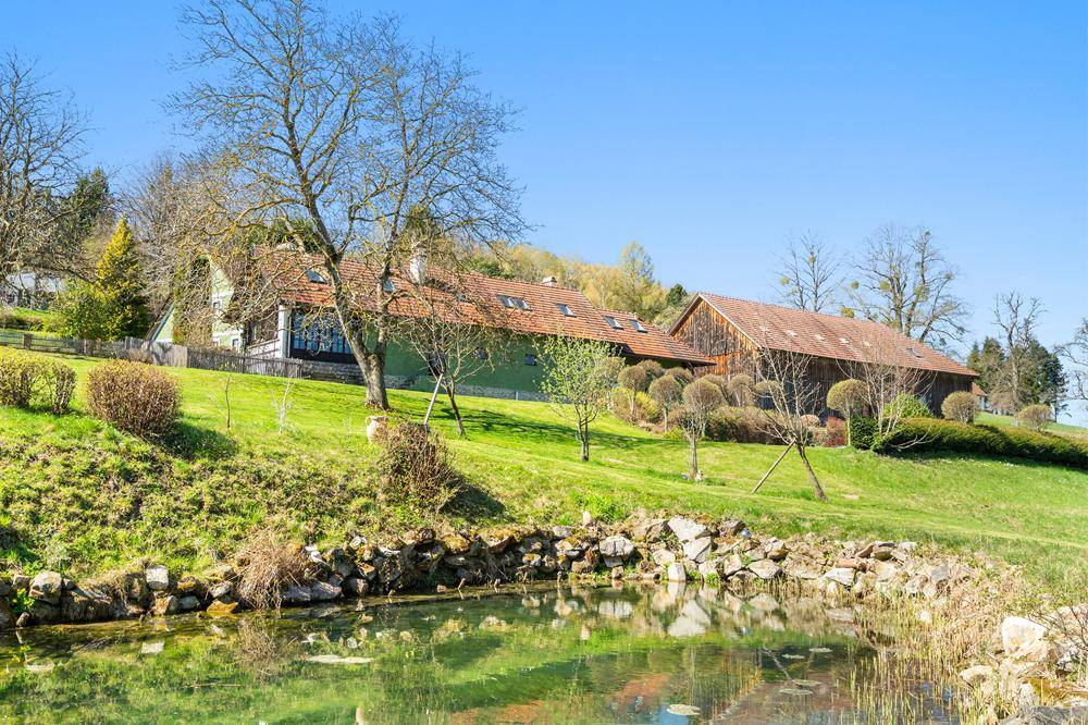 Idyllische Landschaft mit einem Teich im Vordergrund und dem Anwesen im Hintergrund.