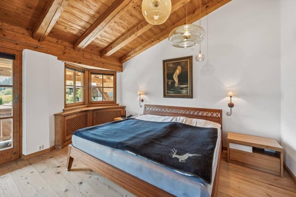 Gemütliches Schlafzimmer mit Holzbalkendecke, Holzboden und Zugang zum Balkon.