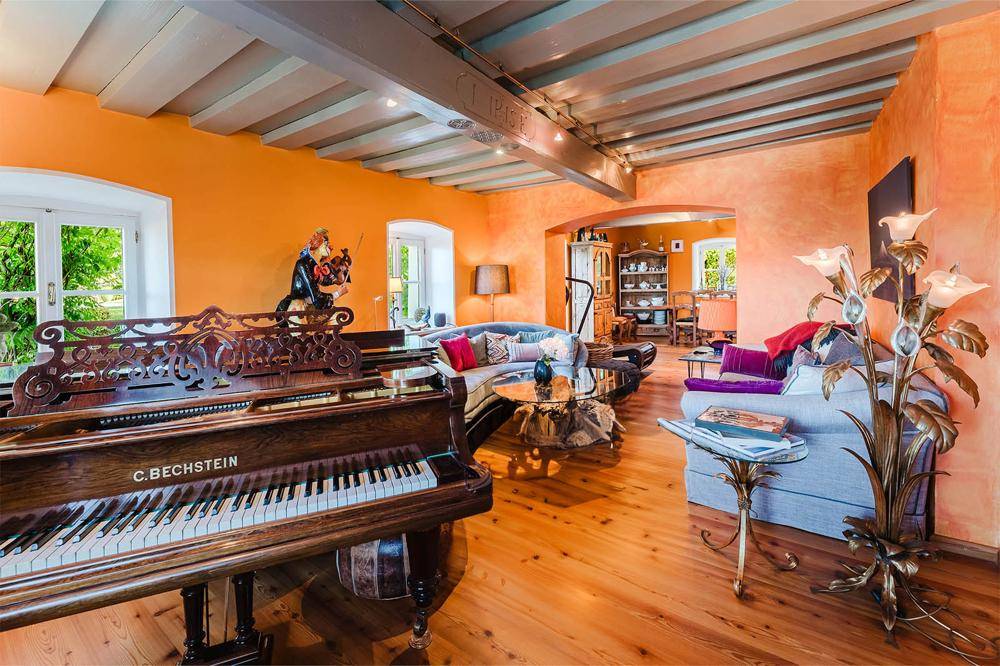 Geräumiges Wohnzimmer mit Holzbalkendecke, Parkettboden und einem antiken Klavier, hell und einladend.