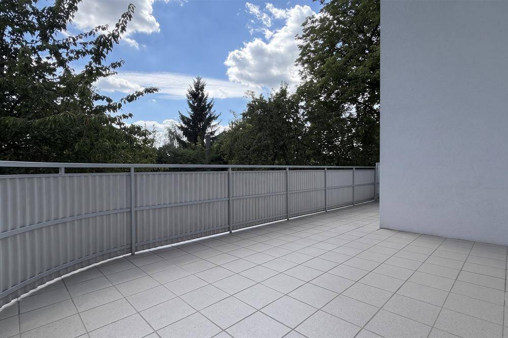 Geräumige, geflieste Terrasse mit Metallgeländer und Blick ins Grüne.