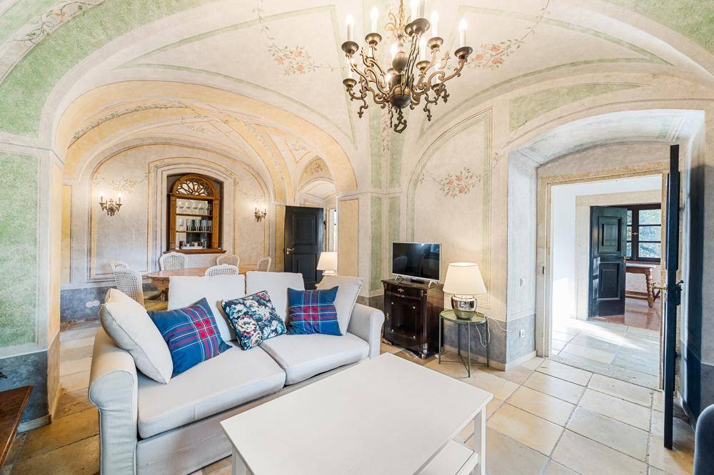 Historisches Wohnzimmer mit kunstvoll bemalten Gewölbedecken, elegantem Kronleuchter und bequemer Couch.