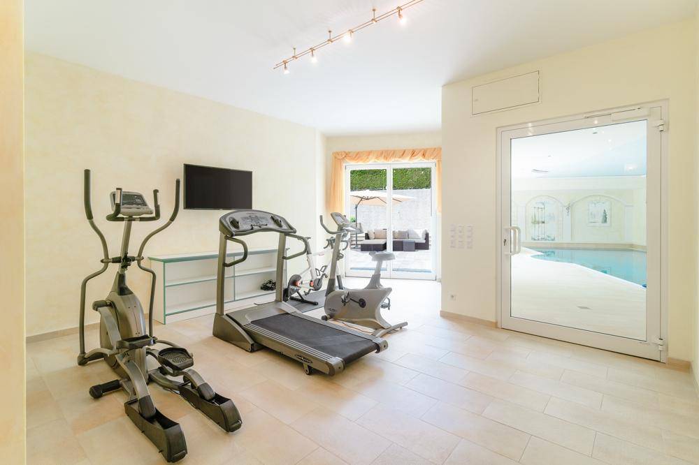 Gut ausgestatteter Fitnessraum mit verschiedenen Trainingsgeräten und Blick auf den Poolbereich.
