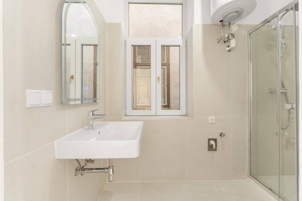 Helles Badezimmer mit moderner Dusche, wandmontiertem Waschbecken und Fenster für natürliche Belüftung.