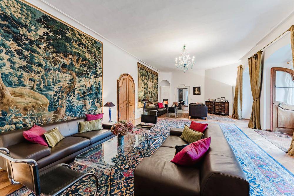 Opulentes Wohnzimmer mit Ledersofas, großem Wandteppich, Kronleuchter und traditionellen Teppichen.