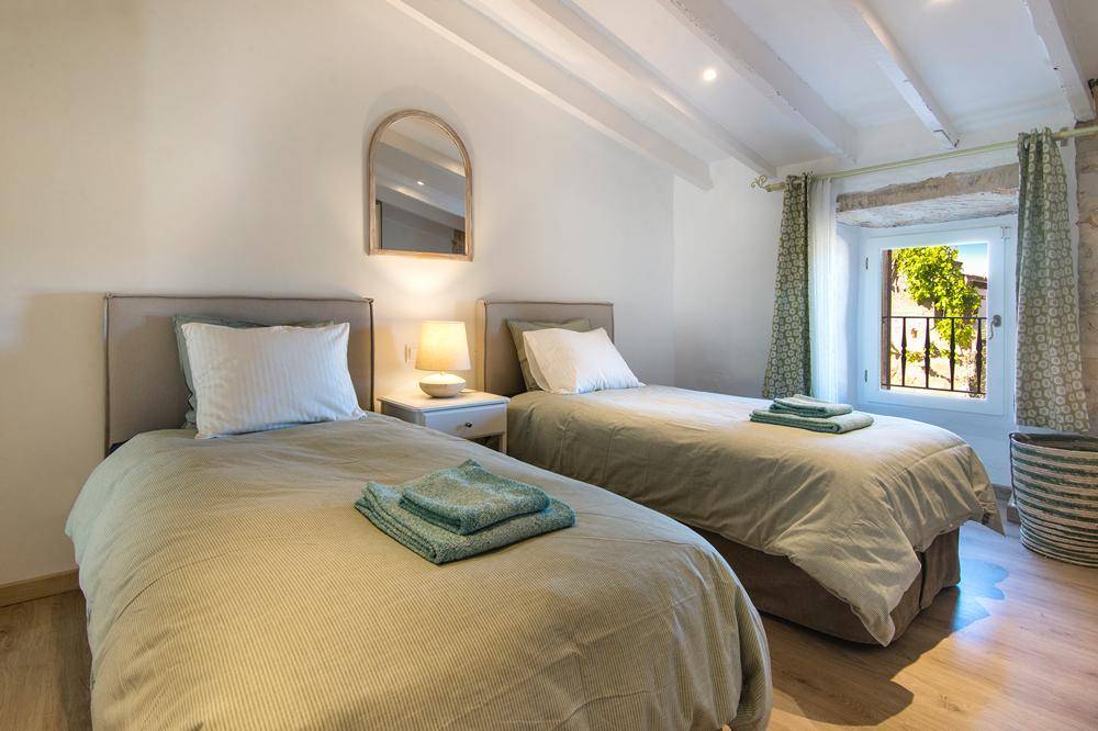 Helles Schlafzimmer mit zwei Einzelbetten, Holzbalkendecke und Blick ins Grüne.