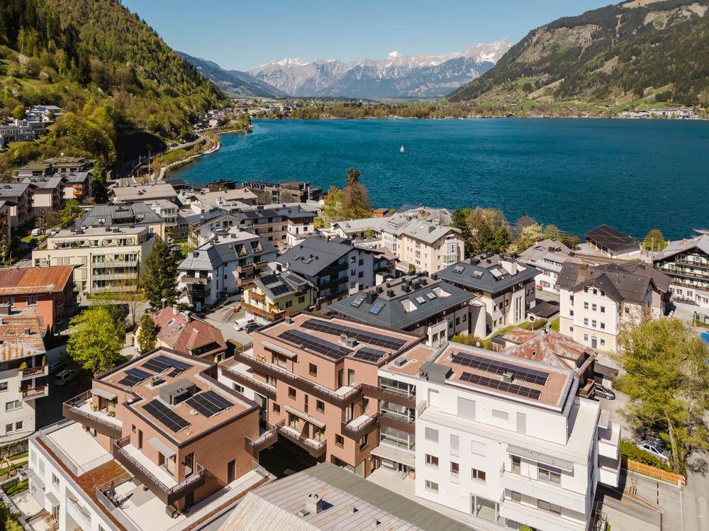 Luftaufnahme einer Stadt am See, umgeben von Bergen, mit modernen Gebäuden und Solaranlagen auf den Dächern.
