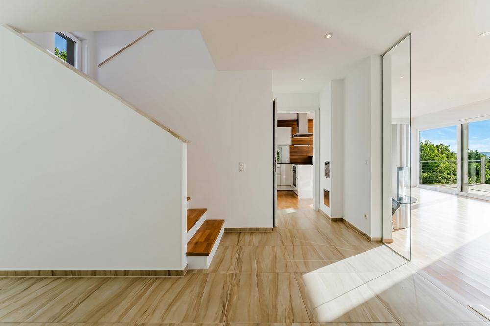 Heller Eingangsbereich mit Holztreppe, Fliesenboden und Blick in die moderne Küche.