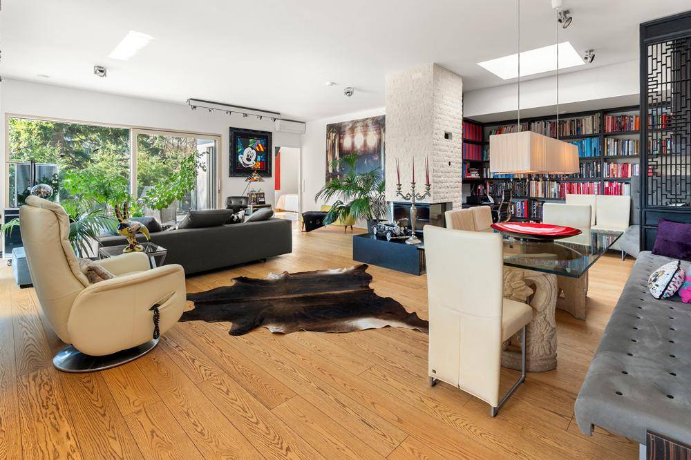 Geräumiges Wohnzimmer mit Kamin, Holzboden und großer Bücherwand, lichtdurchflutet.