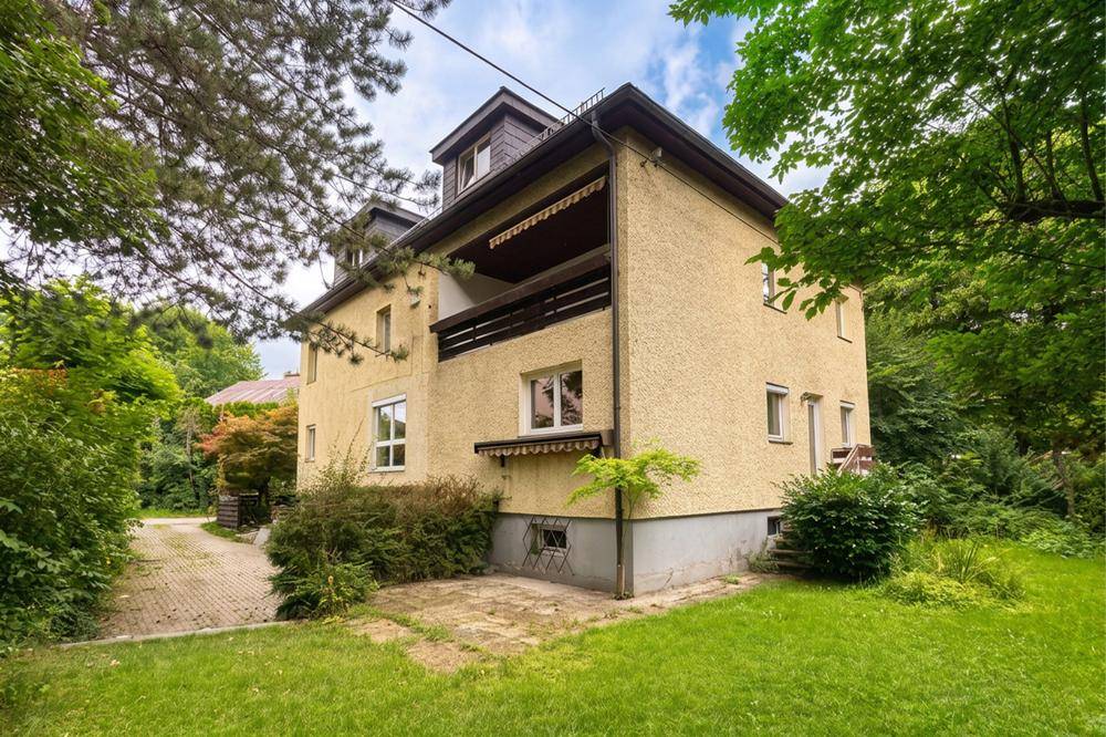 Gelbes Wohnhaus mit Balkon, Dachgauben und weitläufigem grünen Garten.